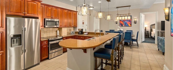 A kitchen with a stainless steel refrigerator, a microwave, a double oven, and a granite countertop island with bar stools.
