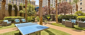 Une cour avec une table de ping-pong, des sièges extérieurs et des palmiers.