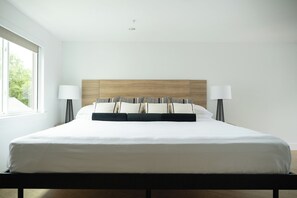 Ein modernes Hotelzimmer mit einem großen Bett, zwei Nachttischlampen und Blick auf Grün.