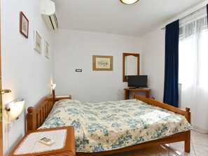 Una camera da letto con un letto, un comodino, una lampada, condizionatore d'aria, televisione e una finestra con tende.