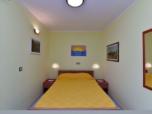 A bedroom with a bed, two bedside tables, a nightstand, a wall-mounted painting, and a ceiling light. - Apartment 372 by Interhome (Medulin)