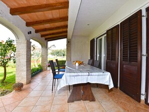 A covered patio area with a table set for two, a wooden bench, and a door with louvered shutters. - Apartment 372 by Interhome (Medulin)