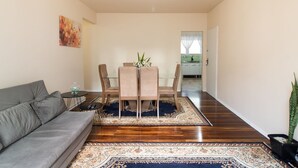 A living room with a gray sofa, a dining table with chairs, and a blue and beige patterned rug. - Apart w/ Side sea View, 50m From the Beach Mrd0061 (Balneário Camboriú)