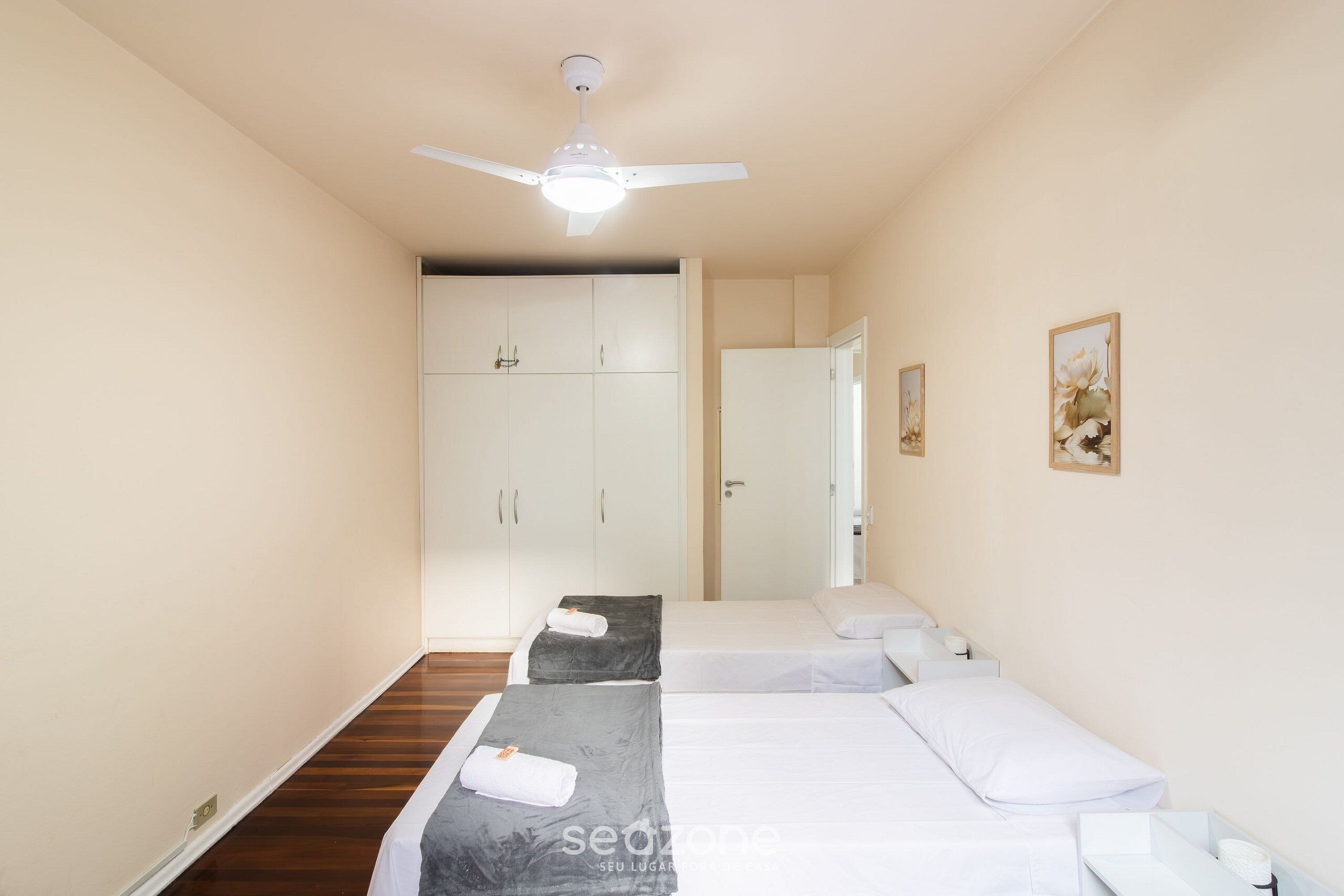 A hotel room with two beds, a ceiling fan, and a wardrobe.