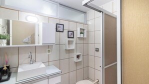 A bathroom with a white sink, mirror, and toilet. There are two framed pictures on the wall, and a small shelf with a plant. - Apart w/ Side sea View, 50m From the Beach Mrd0061 (Balneário Camboriú)