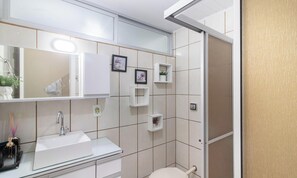 Un baño moderno con lavamanos, espejo y paredes con azulejos. Se ven pequeñas repisas con plantas y un inodoro.