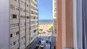 Blick auf einen Strand von einem Hochhaus mit mehreren Etagen und Balkonen, mit Blick auf einen Sandstrand mit Sonnenschirmen und Menschen.