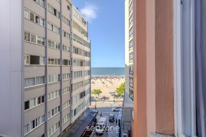A view of a beach from a high-rise building with multiple floors and balconies, overlooking a sandy beach with umbrellas and people. - 3BR Apt Sea View Balcony in BC Mrd0051 (Balneário Camboriú)