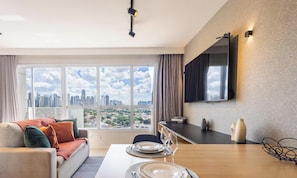A modern living room with a sofa, dining table set, and a large window with a city view. - Full Studio in Jardim Goias Msst1001 (Goiânia)