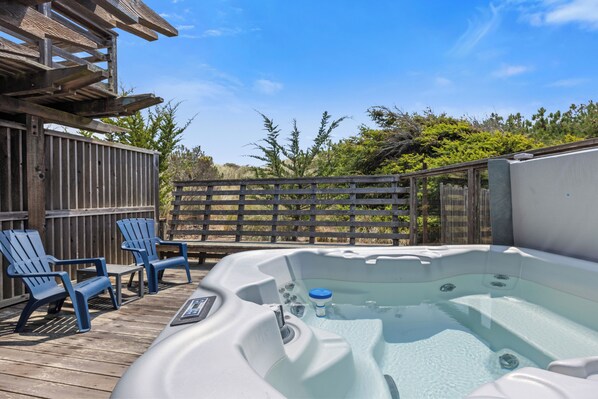 A hot tub on a wooden deck with two blue chairs, surrounded by a wooden fence and greenery. - Miwok Escape, by Vinifera Homes (Bodega Bay)
