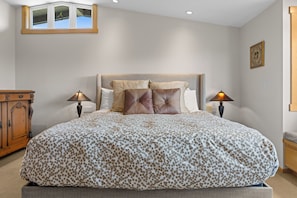 A bedroom with a large bed, two bedside lamps, a wooden cabinet, and a window with a view. - Miwok Escape, by Vinifera Homes (Bodega Bay)