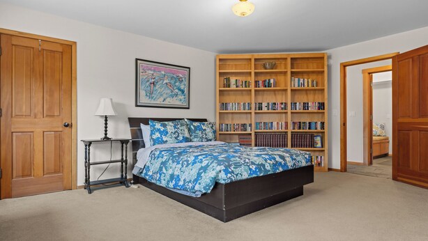 A bedroom with a bed, a nightstand, a lamp, a bookshelf, and a door. - Miwok Escape, by Vinifera Homes (Bodega Bay)