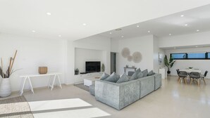 Ein modernes Wohnzimmer mit einem grauen Ecksofa, einem Flachbildfernseher und einem Essbereich mit Tisch und Stühlen.