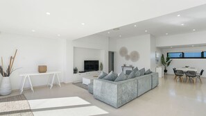 Uma sala de estar moderna com um sofá modular cinza, uma televisão de tela plana e uma área de jantar com mesa e cadeiras.