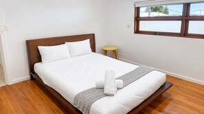 A bedroom with a wooden bed, white bedding, a small stool, and a window with a view. - Dea-Del-Mare 6BR Sleeps 18 Beach Front (The Entrance North)