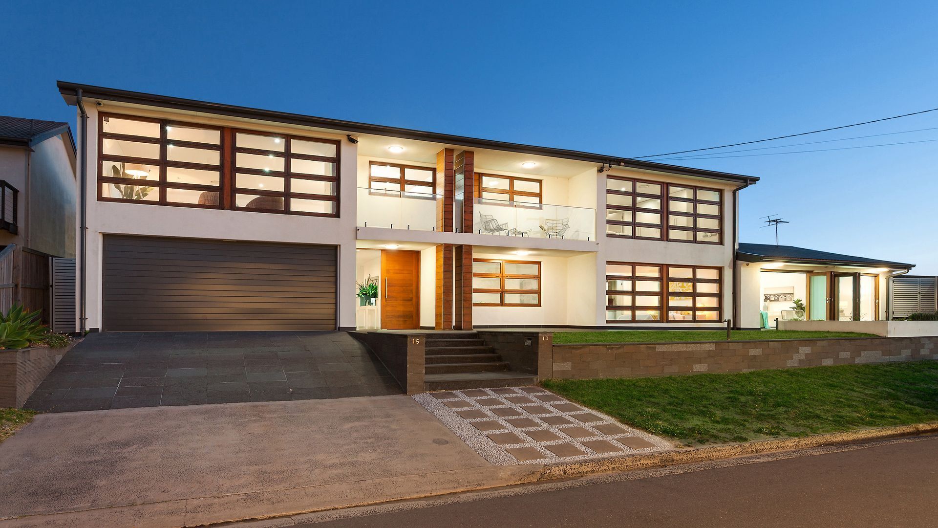 A modern two-story house with a garage, a balcony, and a well-lit entrance.