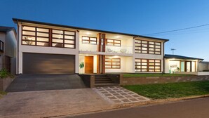 A modern two-story house with a garage, a balcony, and a well-lit entrance.
