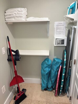 A laundry area with a red vacuum cleaner, folded towels on a shelf, a safety operation sign, and a wall-mounted iron. - Oceanfront Sunrise Escape Condo | Beach and Pool (Fort Lauderdale)
