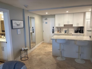 A modern kitchen with white cabinets, a marble countertop, and a bar stool. - Oceanfront Sunrise Escape Condo | Beach and Pool (Fort Lauderdale)