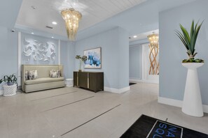 A modern interior with a light blue wall, a beige sofa, a white console table, and a large plant. - Downtown Naples Escape | Resort Pool | Luxury Condo (Naples)