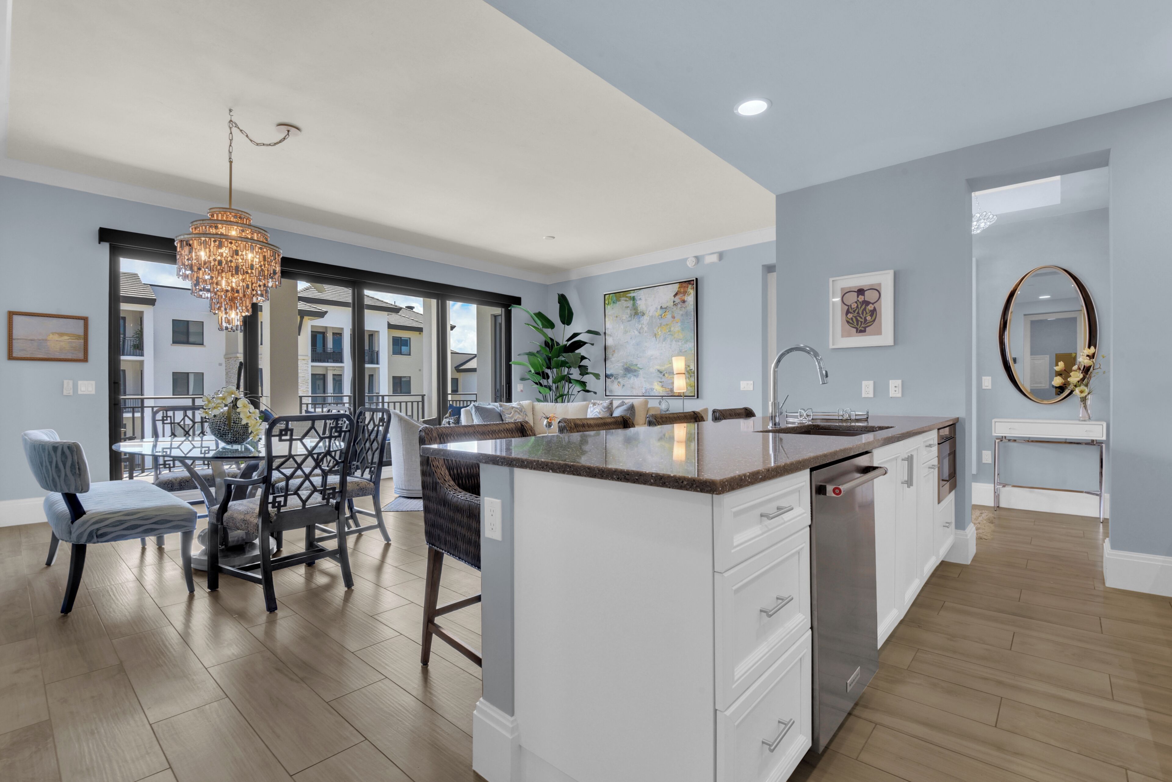 A modern kitchen with a central island, a dining area with a chandelier, and a view of the outside.