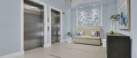 A modern lobby with two elevators, a beige sofa, a decorative wall, and a dark wooden console.