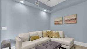 A living room with a sectional sofa, a small table, and two paintings on the wall. - Downtown Naples Escape | Resort Pool | Luxury Condo (Naples)