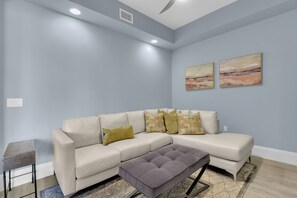 Ein Wohnzimmer mit einem Ecksofa, einem kleinen Tisch und zwei Bildern an der Wand.