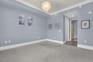 A spacious room with a grey carpet, light blue walls, and a chandelier. There are three framed artworks on the wall. - Downtown Naples Escape | Resort Pool | Luxury Condo (Naples)