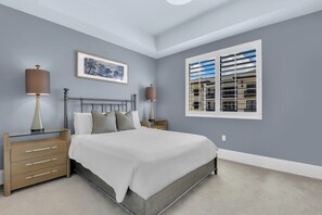 A bedroom with a bed, two bedside tables, a nightstand, a window with blinds, and a framed picture on the wall. - Downtown Naples Escape | Resort Pool | Luxury Condo (Naples)