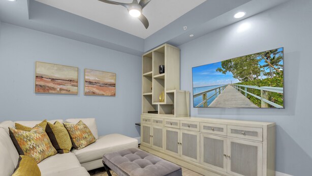 A living room with a white sofa, patterned cushions, a grey ottoman, a white cabinet with shelves, and two landscape paintings. - Downtown Naples Escape | Resort Pool | Luxury Condo (Naples)