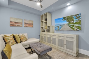 A living room with a white sofa, patterned cushions, a grey ottoman, a white cabinet with shelves, and two landscape paintings. - Downtown Naples Escape | Resort Pool | Luxury Condo (Naples)