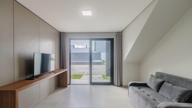 Una sala de estar moderna con un televisor de pantalla plana sobre un mueble de madera, un sofá gris y un ventanal corredizo que da a un espacio al aire libre.