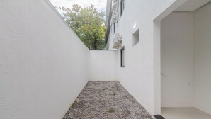 Un espacio exterior pequeño y cerrado con suelo de grava, paredes blancas y una ventana.