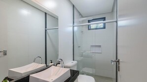Un baño moderno con cabina de ducha de vidrio, inodoro y lavabo doble sobre encimera negra.