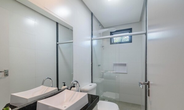 Een moderne badkamer met twee wasbakken, een toilet en een douche met glazen wand.