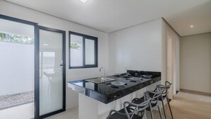 Una cocina moderna con encimera negra, pileta de acero inoxidable y estufa a gas. Hay dos sillas y una ventana con vistas a zonas verdes.