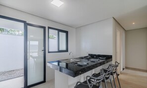 Een moderne keuken met een centraal eiland, barkrukken en een glazen deur naar een buitenruimte.