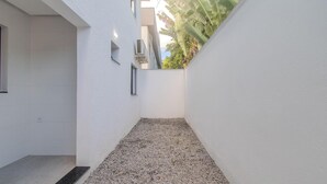 A narrow corridor with white walls, a gravel floor, and a window on the left. - Apart in Condo w/ Barbecue 700m From Beach Nvm0009 (Porto Seguro)