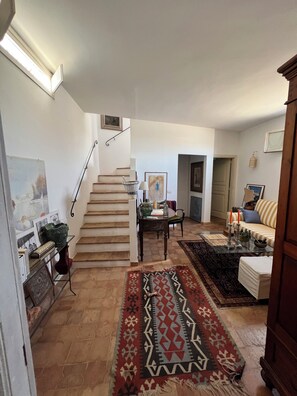 A staircase leading to a second floor, a dining area with a table and chairs, and a living room with a sofa and a patterned rug. - la torretta 23 (Marittima)