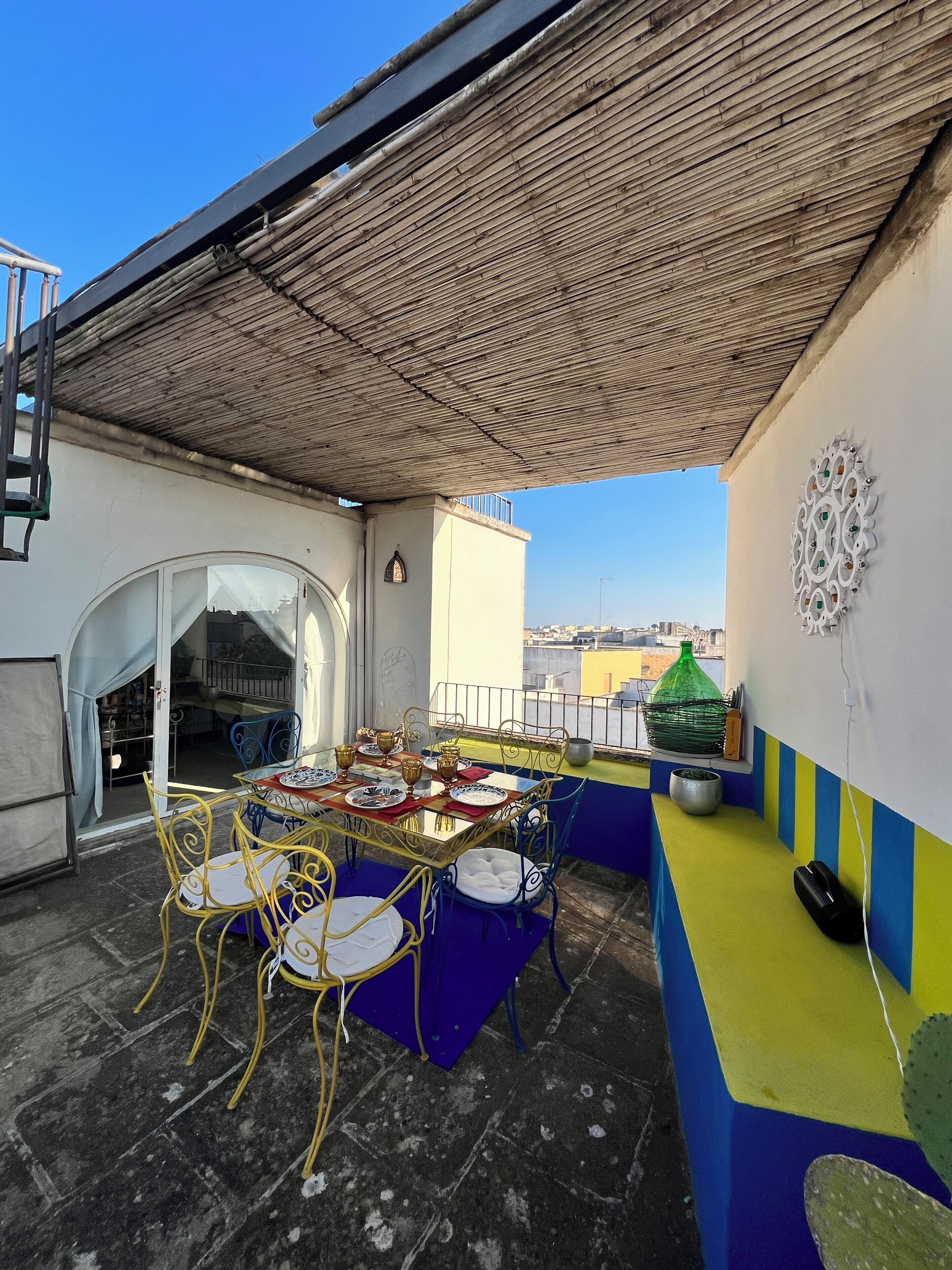An outdoor patio with a table set for dining, chairs, and a decorative wall piece.