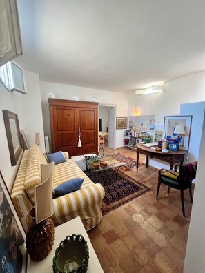A living room with a sofa, a wooden cabinet, a dining table with chairs, and a patterned rug. - la torretta 23 (Marittima)