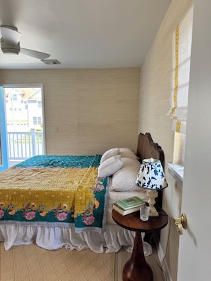 A bedroom with a bed, pillows, a bedside table with a book and a lamp, a ceiling fan, and a window with curtains. - Bright and Sunny Beach House (Ventnor City)