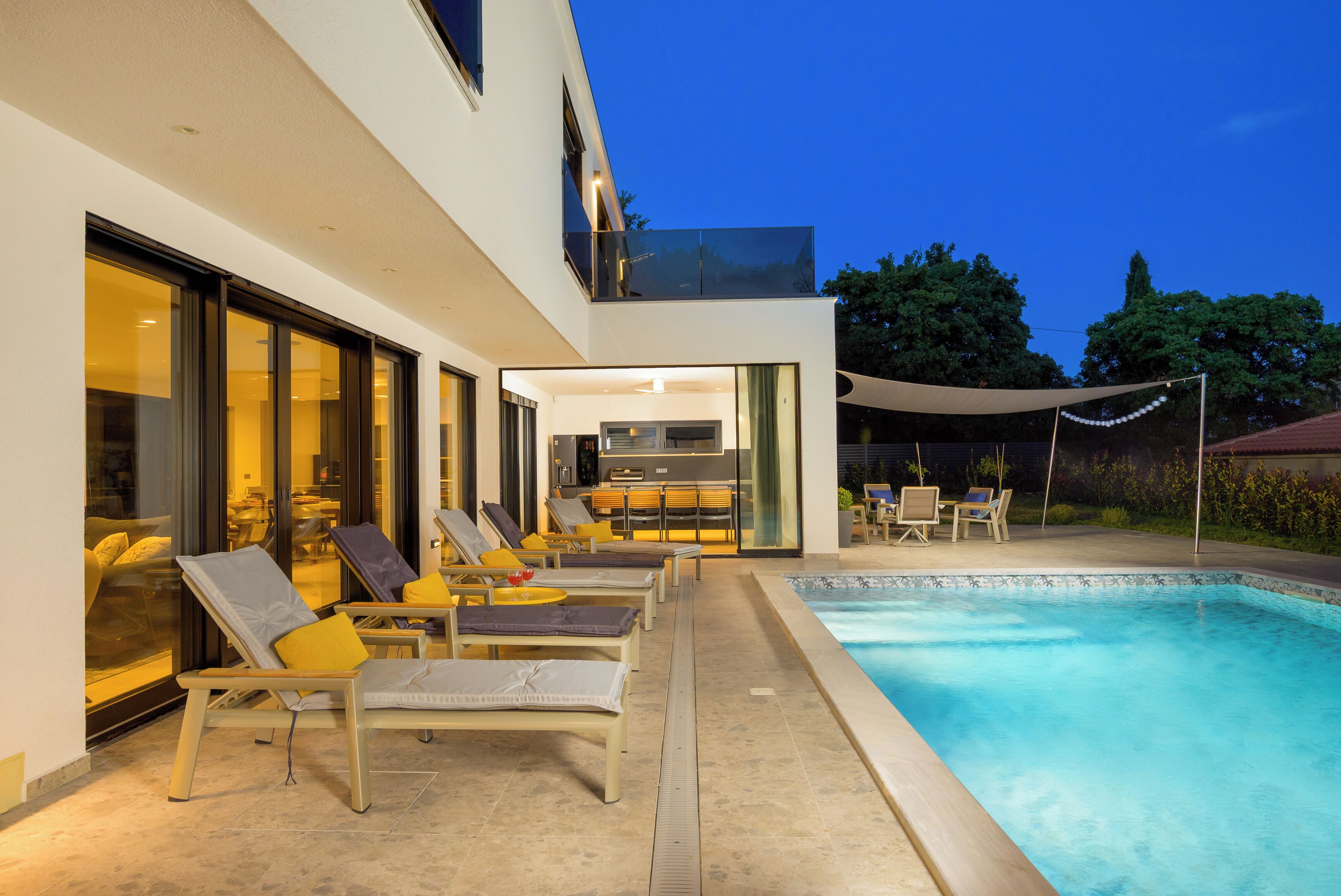 Un espace piscine extérieur moderne, doté de chaises longues et d’un coin repas.