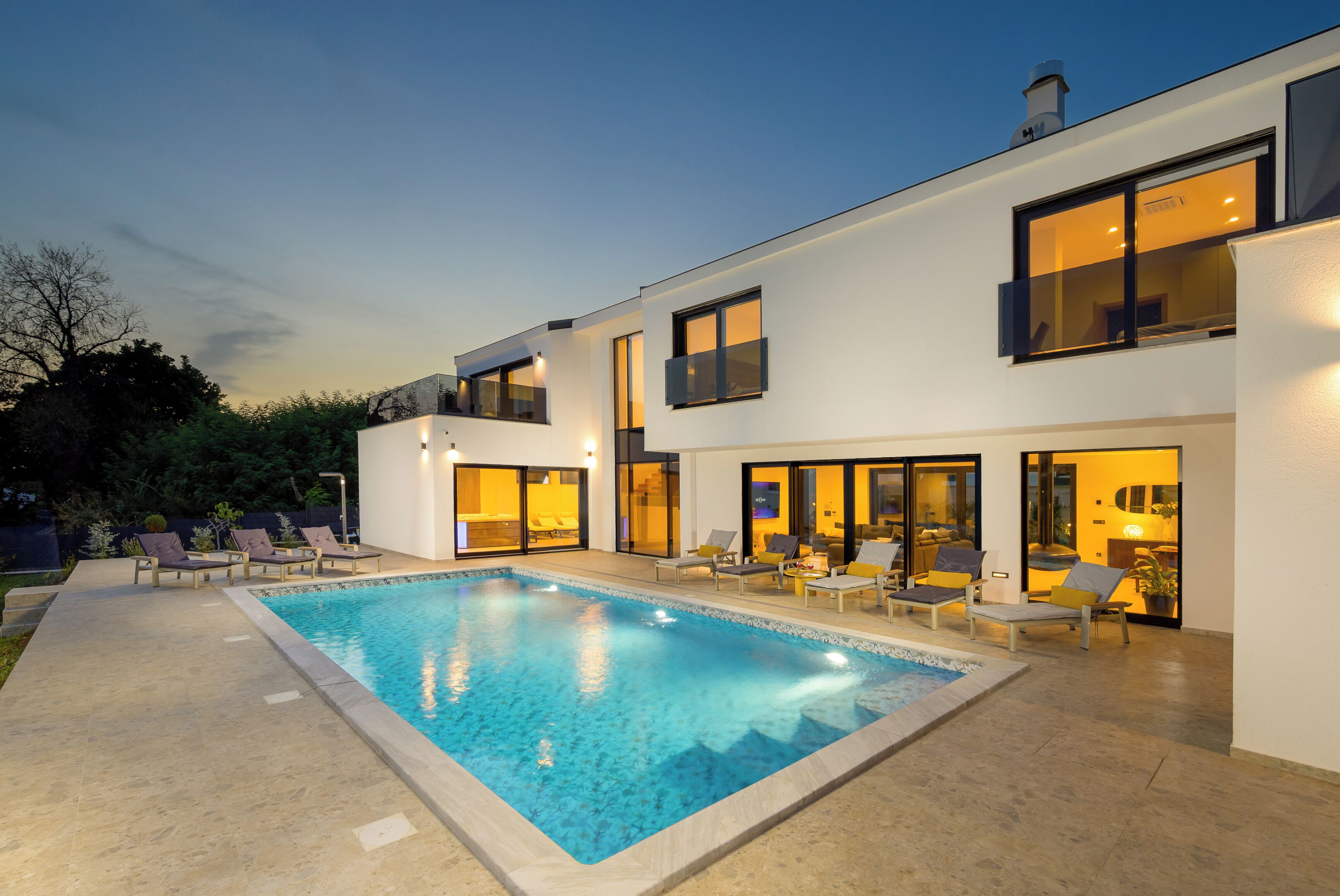 Ein modernes, zweistöckiges Haus mit Swimmingpool, Sitzgelegenheiten im Freien und großen Fenstern.