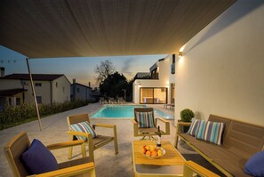 Ein Poolbereich mit Liegestühlen, einem Tisch mit Früchten und Blick auf die umliegende Nachbarschaft.