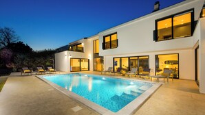 Una casa moderna de dos pisos con piscina, mobiliario exterior y ventanas amplias.