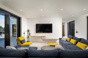 Un salon moderne avec un téléviseur à écran plat fixé au mur, un ensemble de canapés, une table basse et une plante en pot.