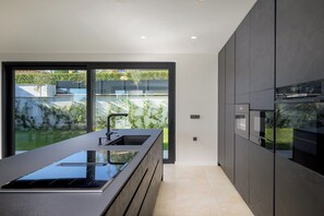 Eine moderne Küche mit einer großen Kochinsel, integrierten Geräten und einer Schiebetür zum Garten.