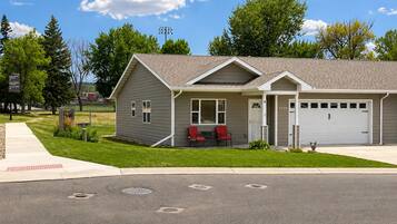 A two-story house with a garage, a covered porch with red chairs, and a well-maintained lawn.